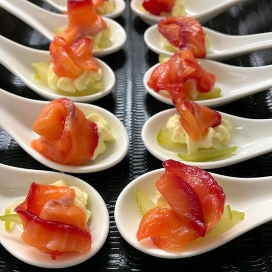 Cured salmon portioned identically across a row of serving spoons.